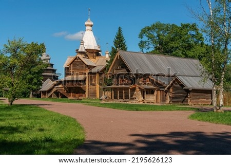 View of the Church of the Assumption of the Virgin and the log house in the Novgorod Museum of Folk Wooden Architecture of Vitoslavlitsa on a sunny summer day, Veliky Novgorod, Russia Royalty-Free Stock Photo #2195626123