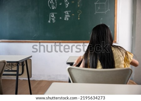 Education. Back view of school girl on lesson in classroom write hardworking on blackboard, primary child is sitting lessons at table in school writing or drawing in notebook, Back to school concept Royalty-Free Stock Photo #2195634273