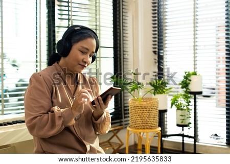 Grandmother listen old music in headphone near piano. Elderly Senior Asian woman enjoy relax from song wireless headset which play oldies songs as think old day and remember cool person, copy space Royalty-Free Stock Photo #2195635833