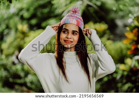 A lovely woman presses , has snow-white teeth. Young girl with brown long hair wearing warm  sweater knit cap and woolen mittens outdoor