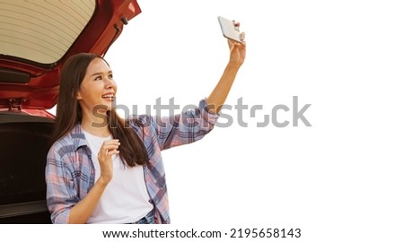 Happy portrait young asian female tourist holding a smartphone takes selfie  looking camera behind her car on white background : Clipping path