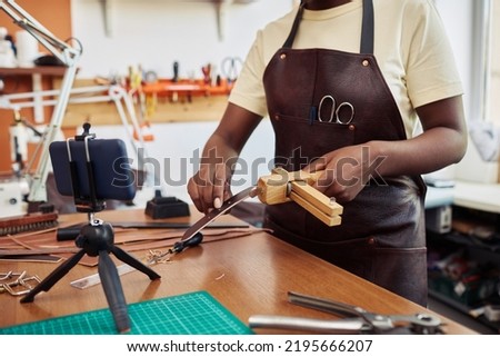 Closeup of young female artisan in leatherworking shop recording video tutorial and promoting small business online