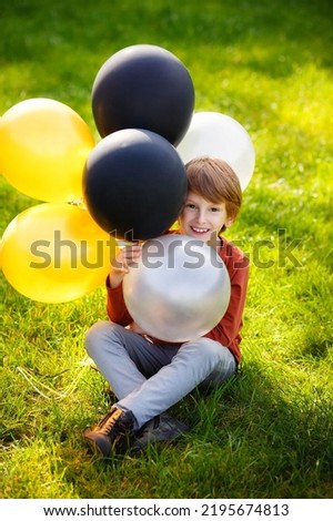 Cute red-haired boy with colorful balloons in a sunny park. The kid is enjoying the game. Happy birthday, festive celebration.