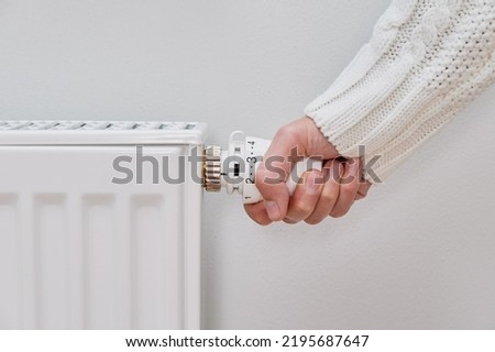 Woman adjusting temperature on heating radiator, Energy crisis concept in Europe, Rising costs in private households for gas bill due to inflation and war Royalty-Free Stock Photo #2195687647