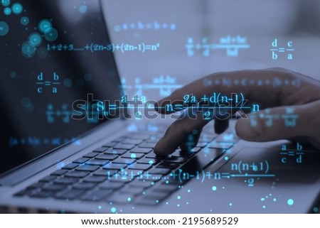Close up of male hands using laptop keyboard at workplace with monitor, supplies and glowing mathematical formulas on blue background. Education, knowledge and statistics concept Royalty-Free Stock Photo #2195689529