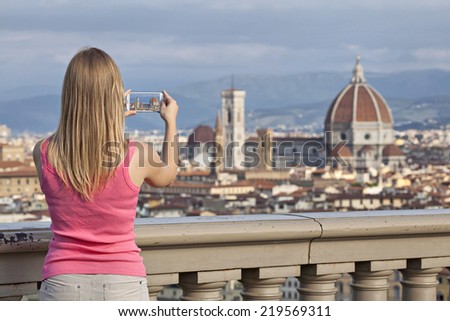 Blonde girl in a pink T-shirt taking a picture of the Florence Cathedral by mobile phone from the observation place