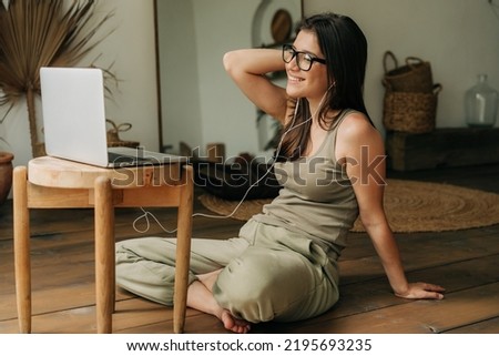 Young brunette woman in eyeglasses at home sitting on the floor using laptop and listening to music Royalty-Free Stock Photo #2195693235