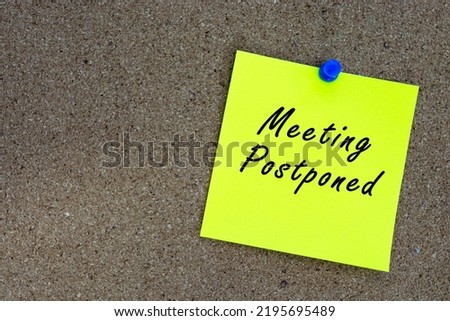 Meeting postponed on yellow stick note and pinned to a cork notice board. Reminder and business concept. Royalty-Free Stock Photo #2195695489