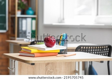 Apple with books, pen cup and school stationery on table in classroom