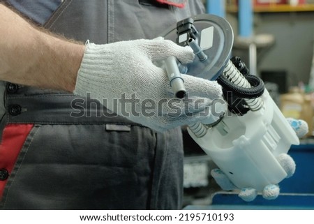 Car maintenance in a car service center. Repair of the fuel and exhaust system of the car. An auto mechanic holds a new fuel pump in his hands, controls its integrity. Royalty-Free Stock Photo #2195710193