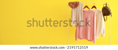 Rack with warm female clothes and accessories on yellow background with space for text
