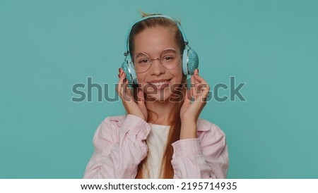 Happy pretty teenager relaxed girl in glasses listening music via headphones and dancing disco fooling around having fun expressive gesticulating hands. Young stylish teen female child kid indoors