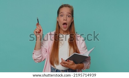 Thoughtful journalist teenager young girl making notes, writing down thoughts with pen into notepad notebook diary, to do list, good idea. Student child kid isolated on blue studio background