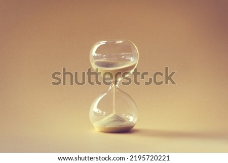Hourglass, also known as sandglass, sand timer, sand clock. Single yellow object on earth colored beige orange paper. Monochromatic background image. Royalty-Free Stock Photo #2195720221