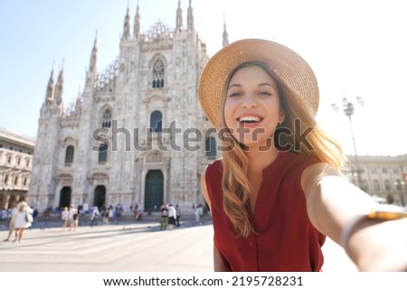 Smiling young woman taking self portrait in the city of Milan, Italy. Laughing girl having fun on vacation in Europe. Tourism and happy lifestyle concept.
