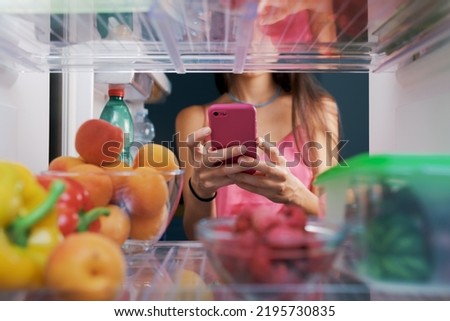 Woman taking pictures of food in the fridge using her smartphone, POV shot from inside of the fridge Royalty-Free Stock Photo #2195730835