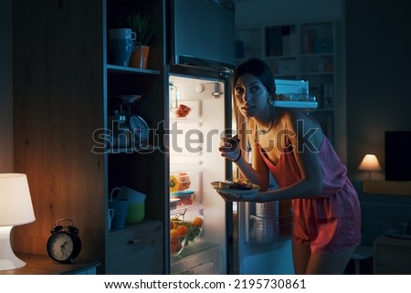 Hungry woman looking in the fridge and eating delicious pastries at night, she is breaking her diet Royalty-Free Stock Photo #2195730861