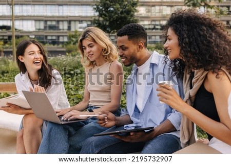 Young diverse university students working away from home on laptop and tablet together. Guy with his girlfriends is discussing new topic sitting on street. Technology concept Royalty-Free Stock Photo #2195732907