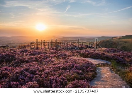 Absolutely stunning sunset landscape image with unidentified couple looking from Higger Tor in Peak District across to Hope Vally in late Summer with heather in full bloom