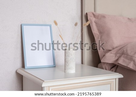 Template with photo frame on a bedside table. Bouquet of Lagurus. Sunlight from the window.