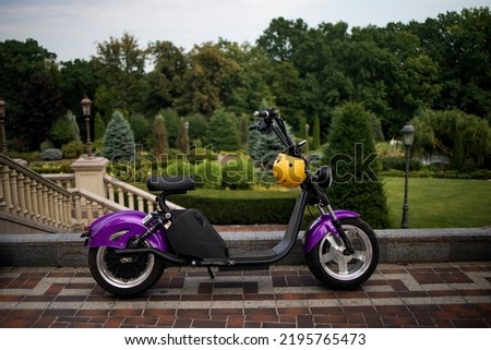 Modern violet electro electric scooter and yellow helmet parking in park Royalty-Free Stock Photo #2195765473