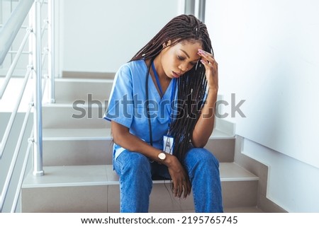Worried and stressed doctor sitting on corridor. Shot of a female nurse suffering from a serious headache while working inside a hospital. Overworked Nurse In Scrubs Takes Coffee Break In Hospital 