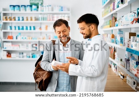 Young pharmacist talking to male customer in a drugstore. Focus is on customer.  Royalty-Free Stock Photo #2195768685