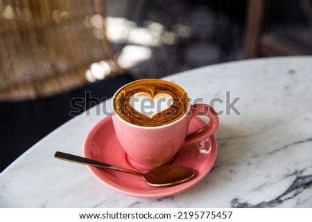 Trendy pink cup of hot cappuccino on marble table background. Heart shape latte art for symbol of love. One cup for morning routine.