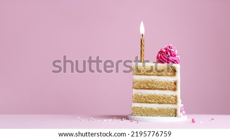 Slice of birthday cake with gold birthday cake candle and pink frosting on a pink background