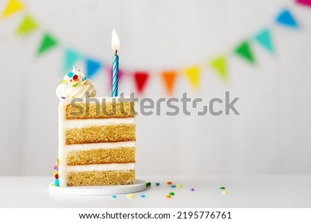 Slice of birthday cake with blue birthday candle, colorful sprinkles and celebration bunting ready for a birthday party