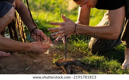 Fire making in the wild (wilderness survival). Two boys trying to make a fire with hand-drill method. Royalty-Free Stock Photo #2195781813