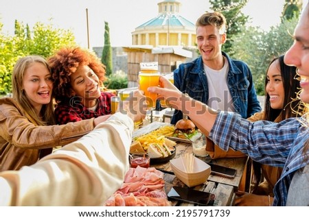 Group of multiethnic friends living healthy lifestyle and smiling and joking while drinking beer at outdoor pub restaurant - Young people toasting with beer glass during happy hour at bar