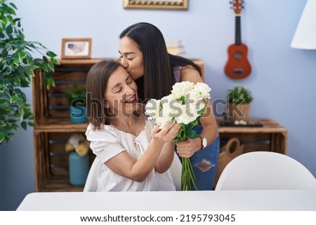 Two women mother and daughter surprise with bouquet of flowers at home