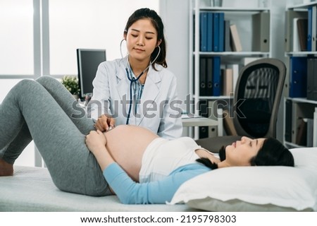 selective focus asian female gynecologist is using stethoscope on the pregnant woman’s belly while listening to baby heartbeat on treatment couch in clinic Royalty-Free Stock Photo #2195798303