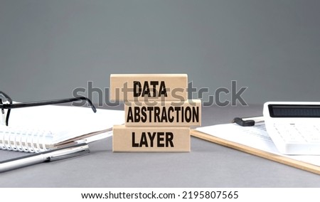 Data Abstraction Layer text on a wooden block with notebook,chart and calculator, grey background