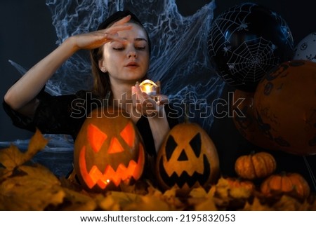 A witch casts a spell in the dark on Halloween on a black background with spider webs, autumn leaves and balloons. Halloween's holiday attributes. Trick or treat.