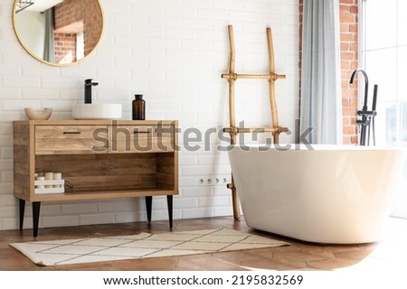 Loft modern style bathroom. Free standing bath and black faucet for water and white separate high sink on wooden pedestal. Royalty-Free Stock Photo #2195832569