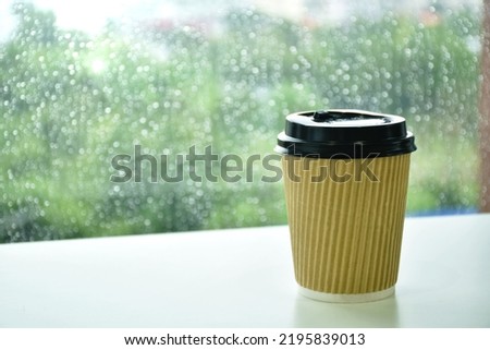 hot coffee in brown plastic cup on glass window in rainy day 