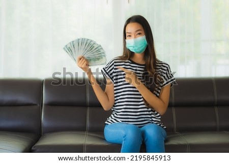 Portrait beautiful young asian woman with mask on sofa show money or cash at home Royalty-Free Stock Photo #2195845913