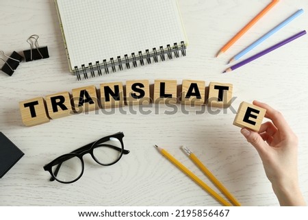 Woman making word Translate with wooden cubes at white table, top view