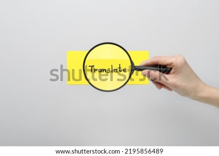Woman holding magnifying glass over sheet of paper with word Translate on light grey background, top view