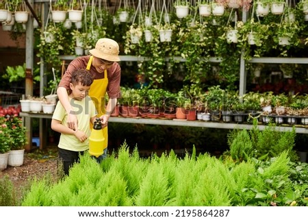 Father teaching son spraying juniper plants at nursery