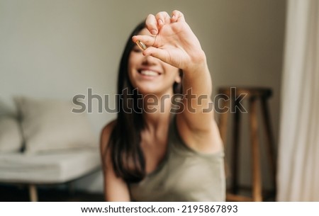 Happy healthy woman recommending omega 3 fish oil and holding out a pill in her hand Royalty-Free Stock Photo #2195867893