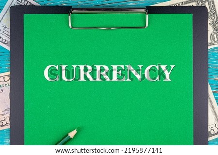 CURRENCY - word (text) and money bills, dollars on a green background notepad, pencil, wooden table. Business concept: buy, sell, commerce (copy space).