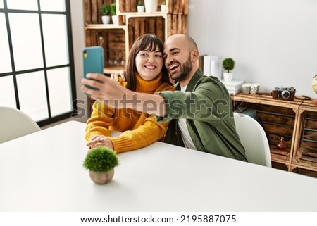 Young hispanic couple smiling happy make selfie by the smartphone sitting on the table at home.