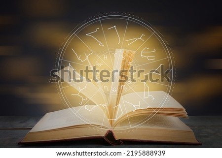 Open book on wooden table and illustration of zodiac wheel with astrological signs