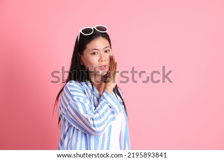 The Asian adult woman with casual clothes standing on the pink background.