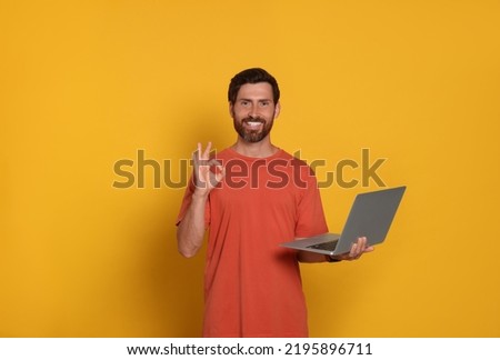 Handsome man with laptop showing OK gesture on orange background