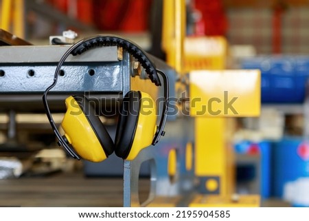 Yellow protective ear muffs hang on machines in heavy industrial plants. The concept is a PPE device that protects against loud noise in the operator's environment. industrial work safety equipment Royalty-Free Stock Photo #2195904585