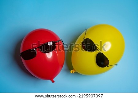 One Red and one yellow balloons with sunglasses on a blue surface